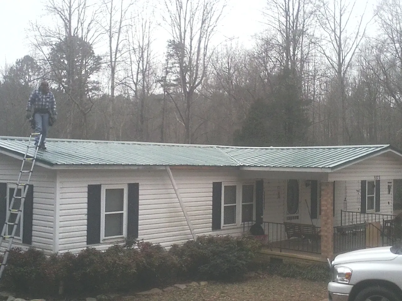 Worker on a ladder beside a new green metal roof on a ranch home in Columbus
